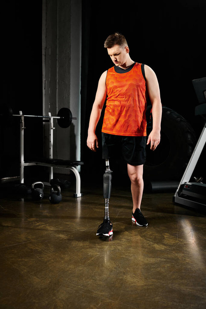 Mies, jolla on proteesijalka, seisoo kuntosalilla liikuntavälineiden ympäröimänä.. - Valokuva, kuva