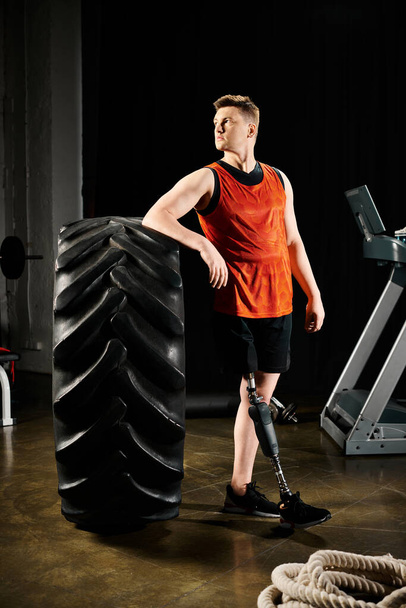 Niepełnosprawny człowiek z protezą nogi stoi dumnie obok dużej opony w siłowni, pokazując swoją determinację i siłę. - Zdjęcie, obraz