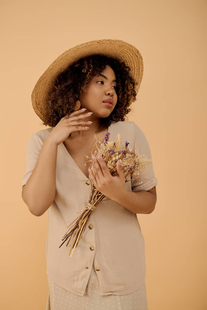 Молода афроамериканка з кучерявим волоссям, одягнена в капелюх, тримає купу квітів в обстановці студії. - Фото, зображення