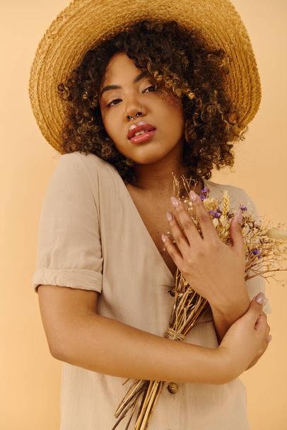 Uma bela jovem afro-americana com cabelo encaracolado usando um chapéu de palha, segurando um monte de flores coloridas. - Foto, Imagem