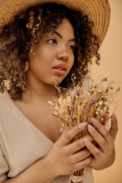A beautiful young African American woman with curly hair, dressed in a summer dress, holding a bunch of dried flowers. - Photo, Image