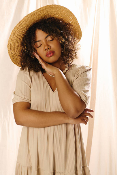 Μια νεαρή Αφροαμερικανή με σγουρά μαλλιά που φοράει ψάθινο καπέλο και καλοκαιρινό φόρεμα αποπνέει αιθέρια ομορφιά σε ένα στούντιο.. - Φωτογραφία, εικόνα