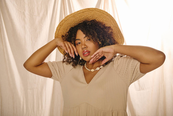 Uma bela jovem afro-americana com cabelo encaracolado vestindo um chapéu de palha e vestido de verão posa graciosamente para uma foto. - Foto, Imagem