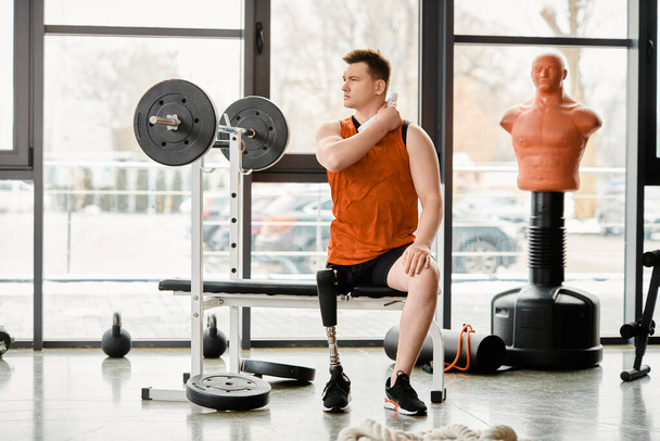 Un hombre discapacitado con una pierna protésica que encuentra consuelo y fuerza mientras se sienta en un banco en un gimnasio, contemplando su entrenamiento. - Foto, imagen
