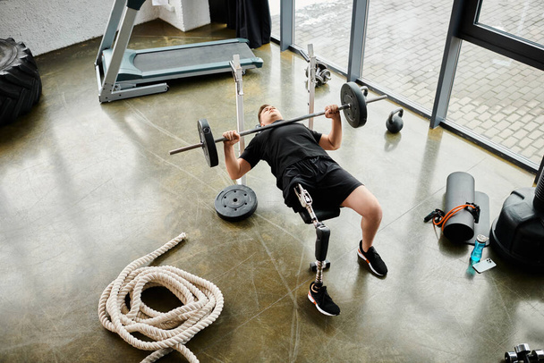 Un hombre con una pierna protésica se involucra en un poderoso callejón sin salida en un gimnasio, mostrando fuerza y determinación. - Foto, Imagen