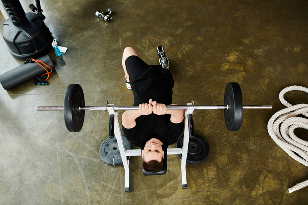 Una persona con una pierna protésica está en un banco, levantando una barra en el gimnasio. - Foto, imagen