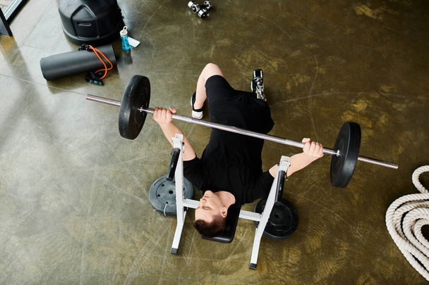 A disabled man with a prosthetic leg lies on the ground, lifting a barbell in a determined and focused manner. - Photo, Image