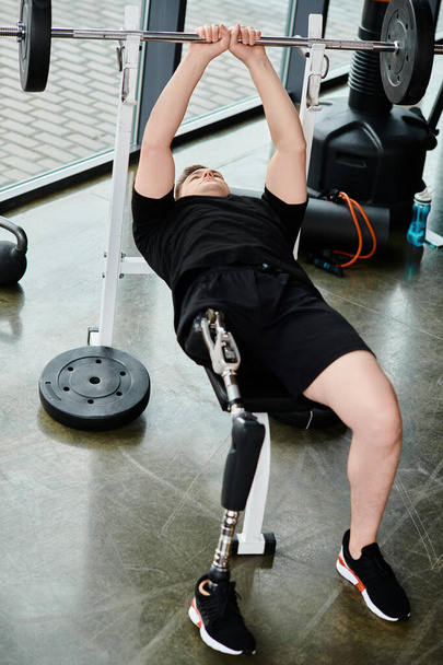 Ein behinderter Mann mit Beinprothese und schwarzem Hemd macht in einem Fitnessstudio eine Kniebeuge mit der Langhantel. - Foto, Bild