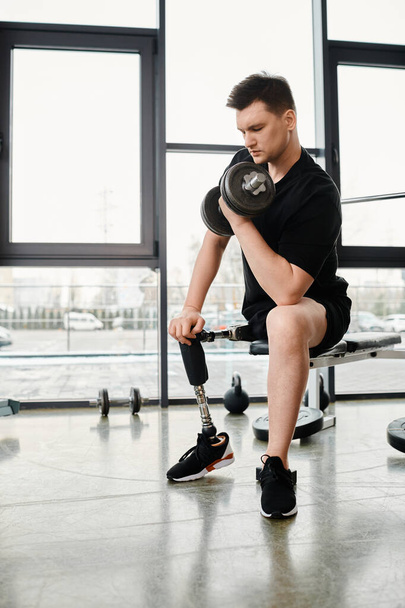 Un hombre con una pierna protésica se sienta encima de un banco sosteniendo una campana de pesas, centrándose en su rutina de entrenamiento en un entorno de gimnasio. - Foto, imagen