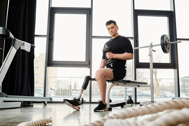 Een man met een kunstbeen wordt gezien zittend op een bank in een sportschool, aan het trainen met halter - Foto, afbeelding