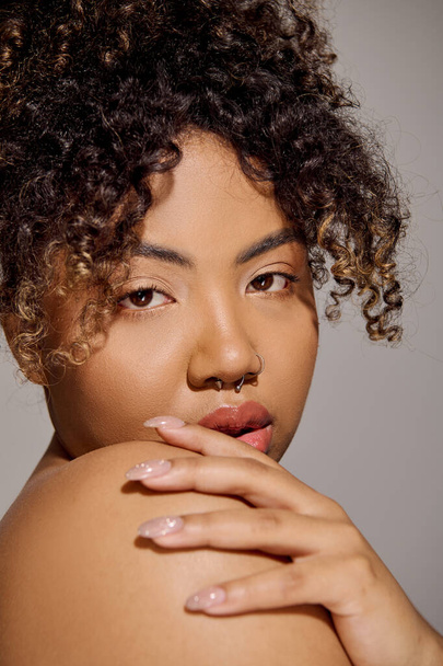 Крупный план ошеломляющей молодой афроамериканки с вьющимися волосами в студии, источающей красоту и уверенность. - Фото, изображение