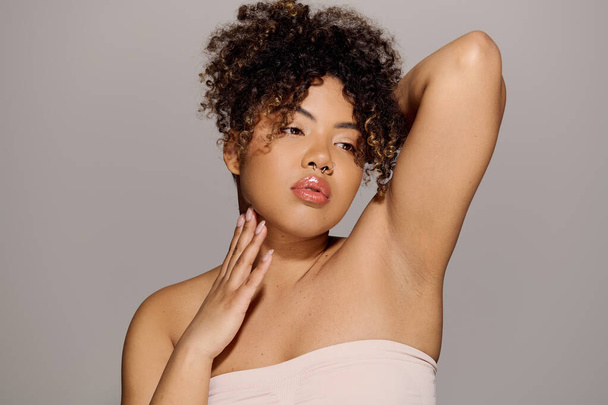 Uma mulher afro-americana deslumbrante com cabelo encaracolado faz uma pose em um ambiente de estúdio, exalando confiança e beleza. - Foto, Imagem