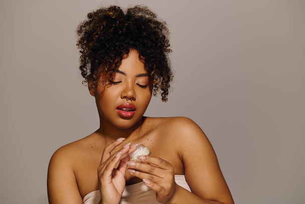Afroamerykanka z kręconymi włosami używająca balsamu do pielęgnacji skóry w studio. - Zdjęcie, obraz