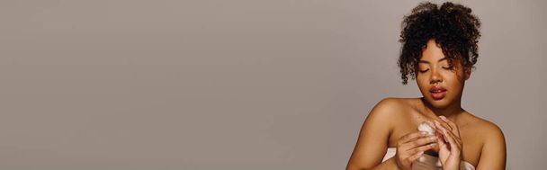 Havluya sarılı kıvırcık saçlı güzel bir Afro-Amerikan kadın stüdyoda zarafet ve zarafet yayıyor.. - Fotoğraf, Görsel