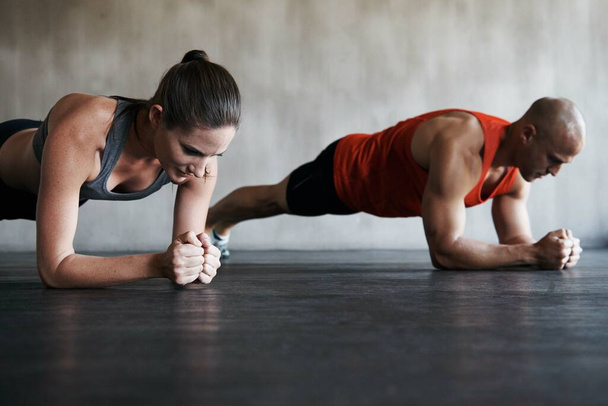 Empuje su camino a la aptitud. Tiro de un hombre y una mujer haciendo ejercicios de tablón en el gimnasio - Foto, Imagen