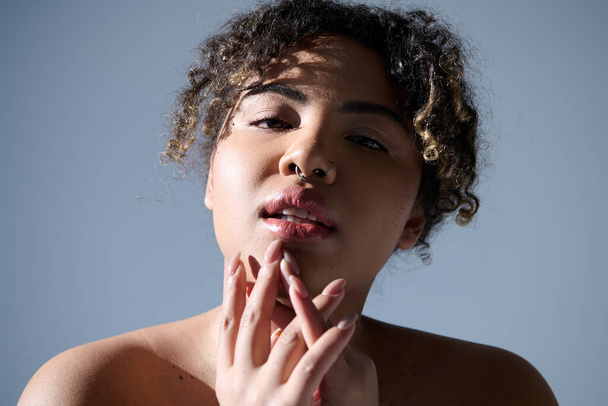 Eine schöne junge Afroamerikanerin mit lockigem Haar, nachdenklichem Gesichtsausdruck und der Hand auf dem Mund in einem Studio-Setting. - Foto, Bild
