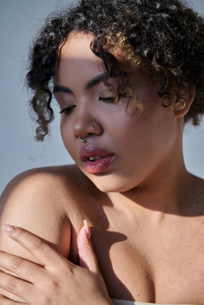 Uma jovem mulher afro-americana deslumbrante com cabelo encaracolado irradiando beleza natural em um ambiente de estúdio. - Foto, Imagem