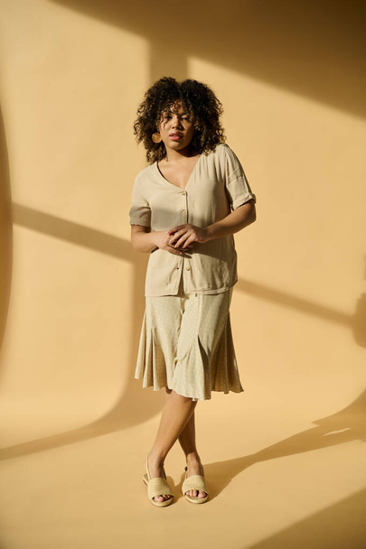 Upea nuori afroamerikkalainen nainen, jolla on kiharat hiukset, seisoo luottavaisesti elinvoimaisen keltaisen seinän edessä.. - Valokuva, kuva