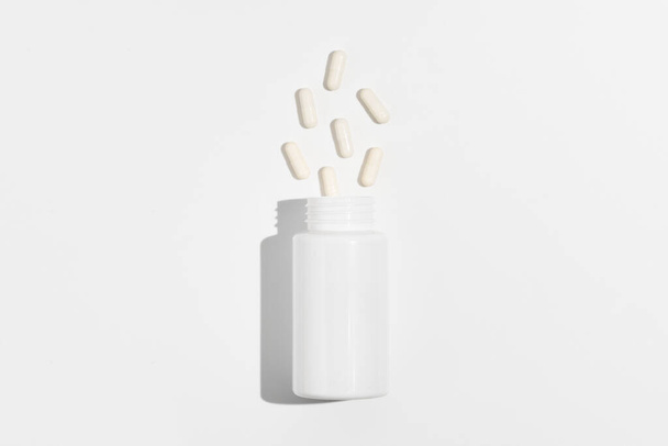 白いバックグラウンドに空白の瓶とこぼされたカプセルの丸薬の白いモックアップ. 薬局,薬局,栄養補助食品,ヘルスケアの概念 - 写真・画像
