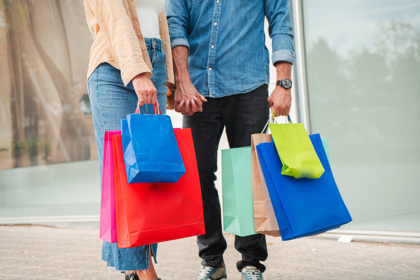 Unrecognizable people carrying shopping bags on a downtown mall. Close up portrait of a couple holding a purchased gift standing on a shop or boutique hall. High quality photo - Photo, Image