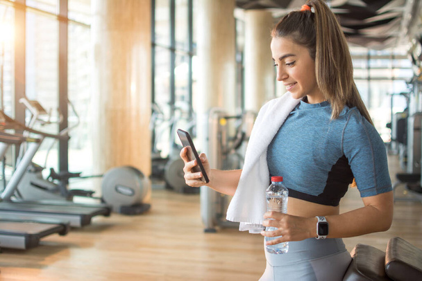 Actief meisje met smartphone in de fitnessruimte. - Foto, afbeelding