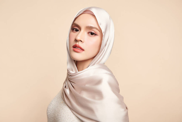 Schöne junge asiatische Muslimin trägt einen weißen Hijab auf beigem Hintergrund, Portrait of Arab Beauty. - Foto, Bild