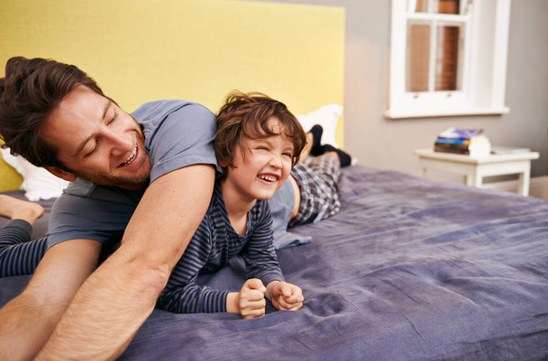 Szczęśliwy, zabawy i ojciec z dzieckiem na łóżku łączenia, relaks i zabawy razem w nowoczesnym domu. Śmiech, uśmiech i młody tata leżący z chłopcem w sypialni w weekend w rodzinnym domu w Kanadzie. - Zdjęcie, obraz