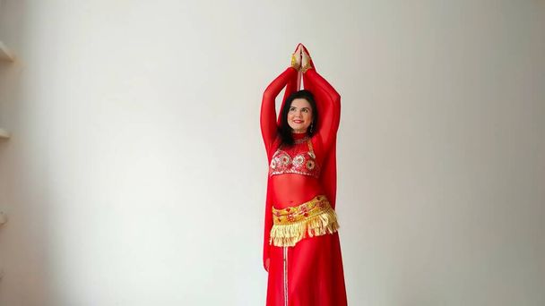 Una bailarina en traje rojo está bailando con un chal rojo una danza oriental sobre un fondo blanco. Espacio libre para texto. Banner. Una bailarina profesional baila danza oriental del vientre. Mujer sexy en vestido rojo - Foto, imagen