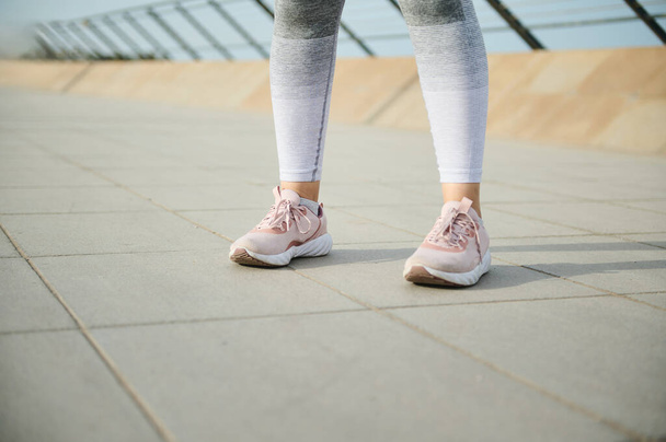Frauenbeine in pinkfarbenen Turnschuhen, Laufschuhen und grauen Leggings auf dem Laufband auf einer Stadtbrücke. Joggen. Körperliche Übungen. Motivation. Gesundheit und Fitness. Ausdauertraining im Freien. Kopierraum - Foto, Bild