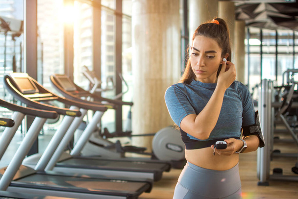 Attractive sporty woman wearing wireless earbuds before training in gym - Photo, Image