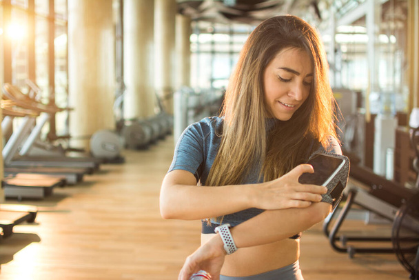 Young fitness woman using phone in armband at gym - Photo, Image