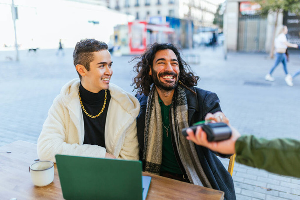 Couple d'hommes souriant tout en effectuant un paiement sans contact avec une carte de crédit dans un café. Paiement, technologie et concept lgbt. - Photo, image