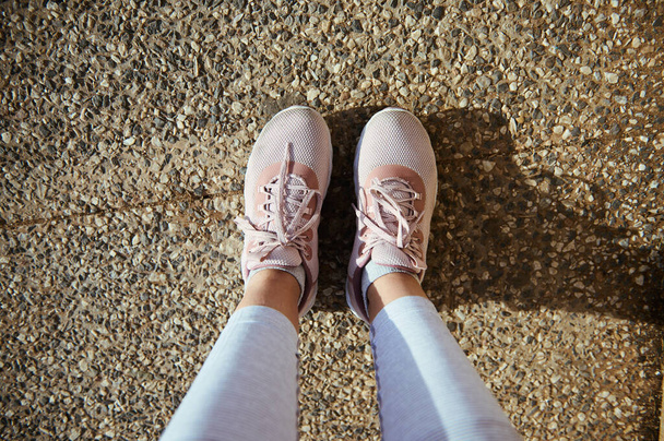 Urheilijanäkökulmasta. Naisurheilijan jalat ja jalat tyylikkäissä urheilukengissä, vaaleanpunaiset lenkkarit asfaltilla. Näkymä ylhäältä urheilullinen tyttö rentouttava jälkeen raskas harjoitus ulkona - Valokuva, kuva