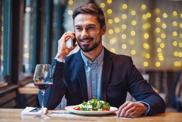 Pohledný podnikatel v obleku je mluvit na mobilním telefonu a usmíval se při posezení v restauraci - Fotografie, Obrázek
