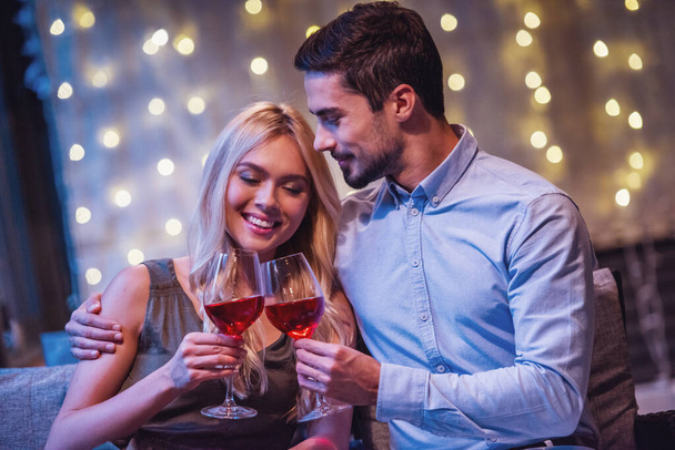 Красивая молодая пара обнимается, пьет вино и улыбается во время свидания в ресторане
 - Фото, изображение