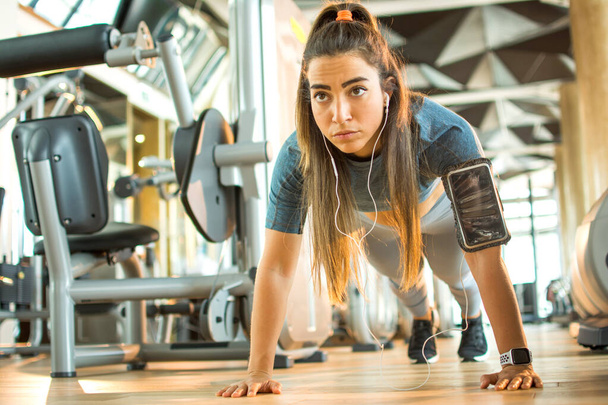 Όμορφη κοπέλα γυμναστικής σε αθλητικά ρούχα προπόνηση κάνει μια σανίδα άσκηση στο γυμναστήριο. - Φωτογραφία, εικόνα