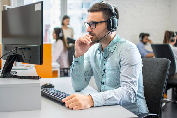 Kundendienstmitarbeiter mit Kopfhörer und Mikrofon hört seinem Kunden im Call Center zu. - Foto, Bild