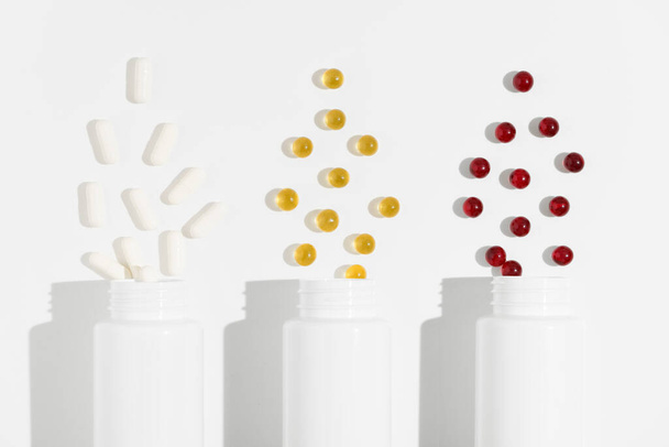 Close-up van drie witte mockup potten met witte, gele en rode capsule pillen op een witte geïsoleerde achtergrond. Concept van de apotheek, voedingssupplementen, gezondheidszorg. Afbeelding voor uw ontwerp - Foto, afbeelding