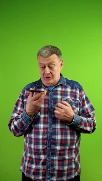 Senior man in shirt holding smartphone and records voice message. Using smart technologies for social media communication, voice commands, messaging. Green screen, chroma key. Vertical. - Footage, Video