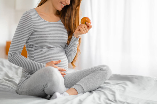 A reflective moment of a pregnant woman looking at an apple, symbolizing healthy food choices during pregnancy - Photo, Image