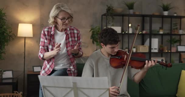 Young man learn how to play violin under instruction of mature woman female professor tutor at home take private class - Footage, Video