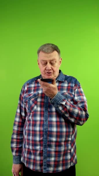 Senior man in casual clothing records voice message with on speakerphone. Using smart technologies to social media communication, voice commands, messaging. Green screen. Chroma key. Vertical. - Footage, Video