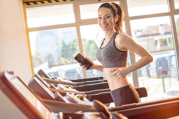 Happy fitness jonge dame draait op loopband machine en genieten van muziek van smart phone. - Foto, afbeelding