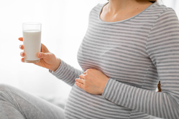 La imagen captura a una mujer embarazada vestida a rayas, sosteniendo un vaso de leche, enfatizando la importancia del calcio durante el embarazo - Foto, Imagen