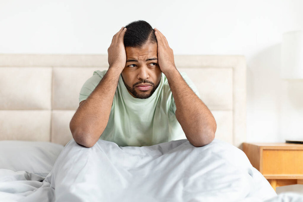 Rozrušený africký Američan trpí bolestí hlavy nebo stresu při sezení v posteli - Fotografie, Obrázek