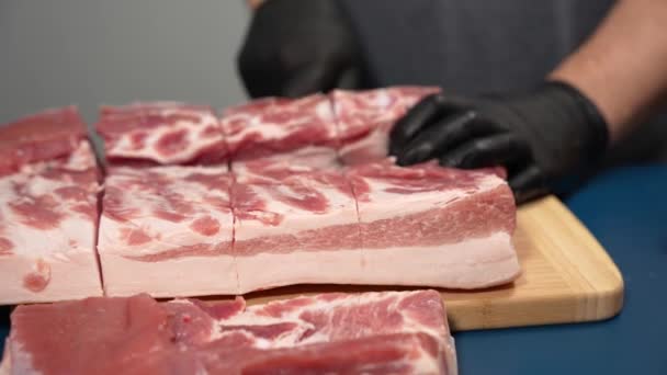 Ein Mann in schwarzen Handschuhen schneidet Schweinefleisch auf einem Schneidebrett. Demonstration der Schweinezucht. - Filmmaterial, Video