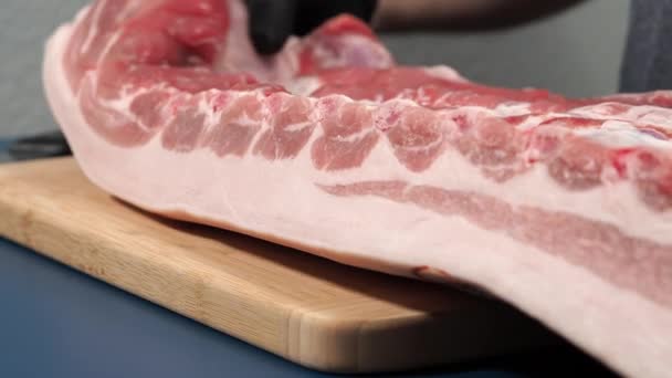 Een man met zwarte handschoenen snijdt varkensvlees op een snijplank. Nauwkeurig snijden van varkensvlees door een ervaren chef. - Video