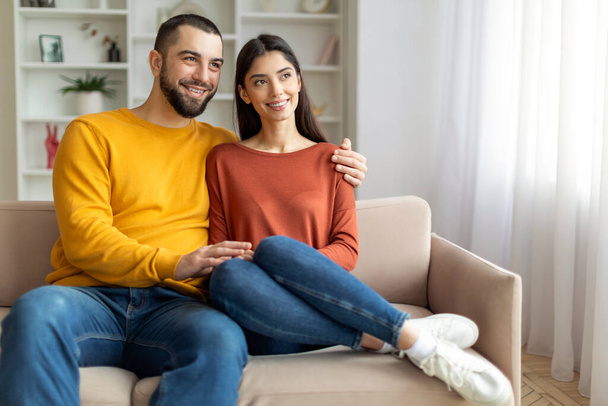 Smiling couple engaging in a conversation on the sofa, radiating positivity - Photo, Image