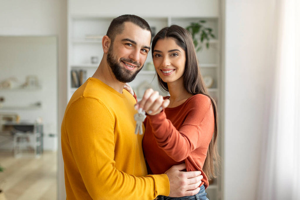 Ένα ζευγάρι με χαρά κρατά τα κλειδιά για ένα νέο σπίτι, ένα σύμβολο μιας νέας αρχής. - Φωτογραφία, εικόνα