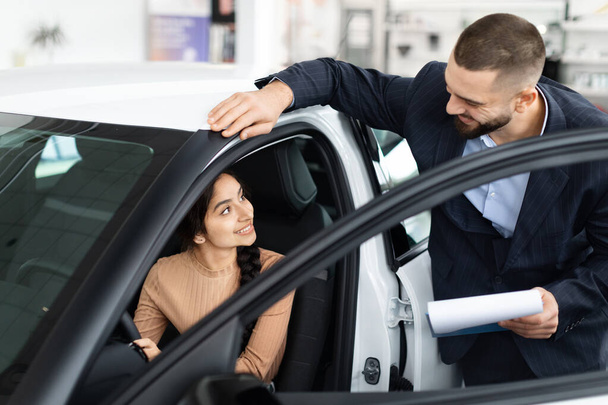 Een professionele verkoper legt voertuig functies aan een geïnteresseerde Indiase vrouw in een auto bij een dealer - Foto, afbeelding
